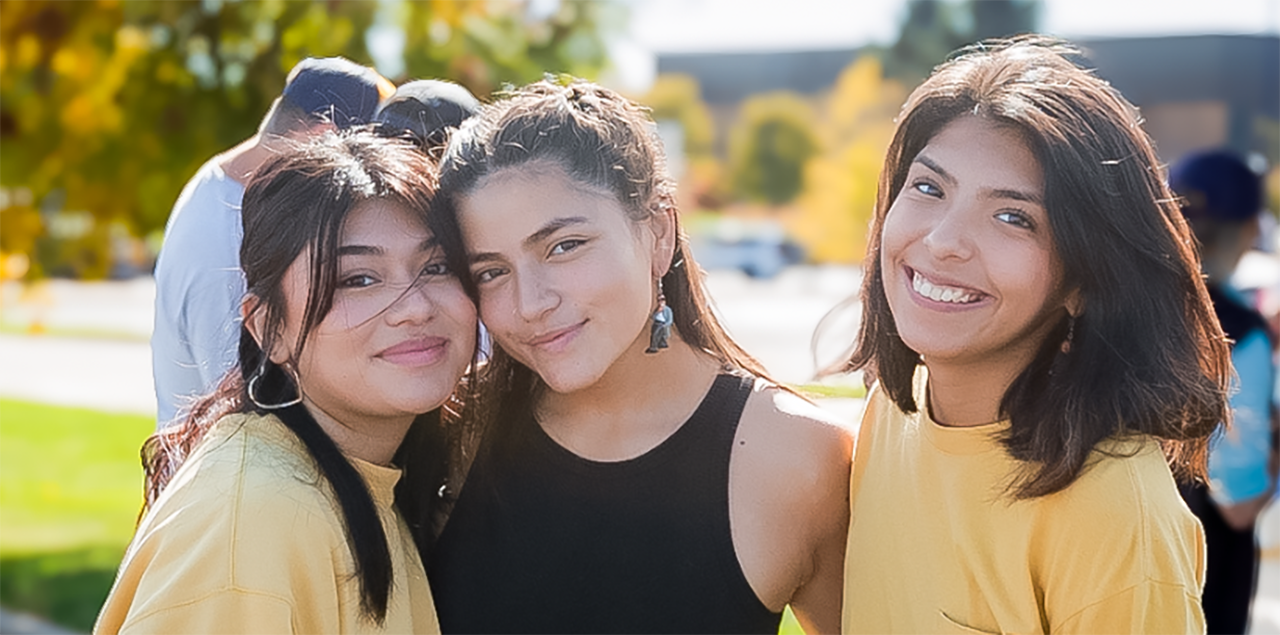 在庆祝西班牙裔/拉丁裔社区的活动中，三名大学生微笑着站在一起